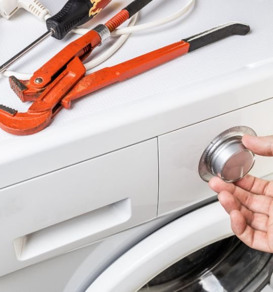 A technician uses a wrench on a washing machine, highlighting laundry appliance repair services in Chicago, IL.