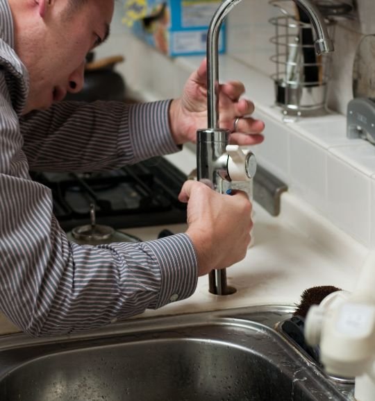A man adjusts a kitchen sink faucet, showcasing small appliance repair services available in Chicago, IL.