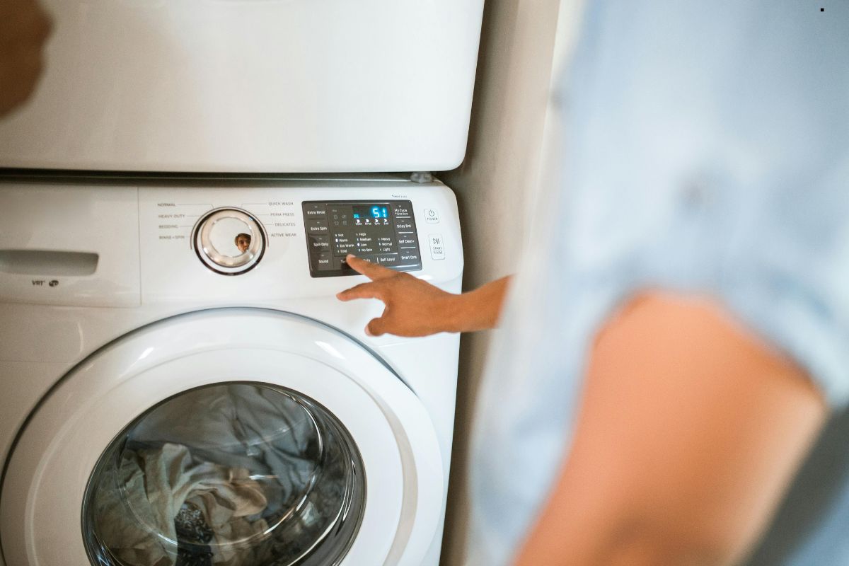 A person points at the control panel of a front-loading washing machine, displaying settings and a countdown timer.