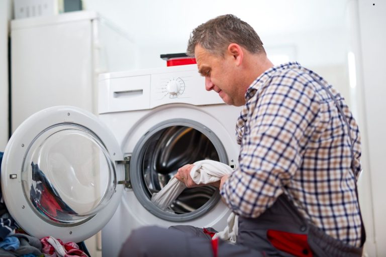A person in a plaid shirt loads a washing machine with white laundry in a bright indoor laundry room.